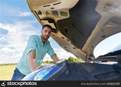 road trip, transport, travel and people concept - young man with open hood of broken car at countryside