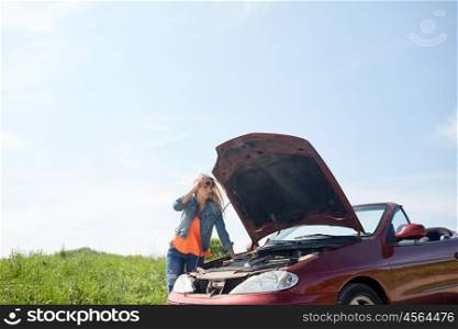 road trip, transport, travel and people concept - young woman with open hood of broken car at countryside