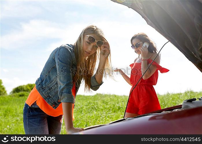 road trip, transport, travel and people concept - young women with open hood of broken car at countryside calling on smartphone to evacuation service