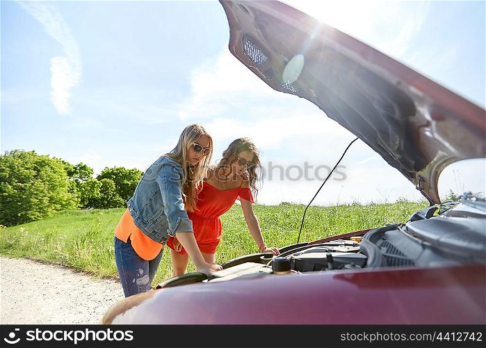 road trip, transport, travel and people concept - young women with open hood of broken car at countryside