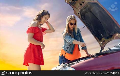 road trip, transport, travel and people concept - young women with open hood of broken car over evening sky background. young women with open hood of broken car. young women with open hood of broken car