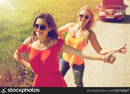 road trip, transport, travel, gesture and people concept - happy young women with broken car showing hitchhiking gesture asking for help at countryside. women with broken car hitchhiking at countryside