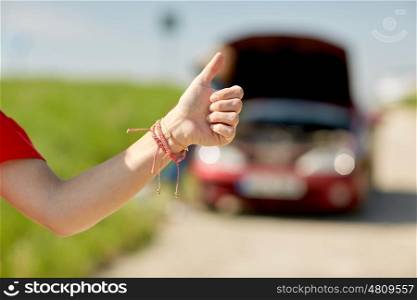 road trip, transport, travel, gesture and people concept - young woman with broken car showing thumbs up and hitching at countryside