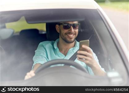 road trip, transport, travel, technology and people concept - happy smiling man in sunglasses driving car with smartphone