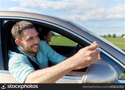 road trip, transport, travel, technology and people concept - happy smiling man with smartphone driving in car and taking selfie