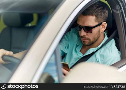 road trip, transport, travel, technology and people concept - man in sunglasses driving car with smartphone