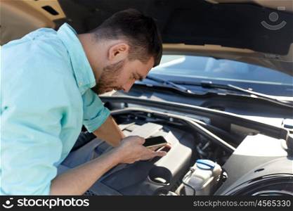 road trip, transport, travel, technology and people concept - young man with smartphone and open hood of broken car at countryside