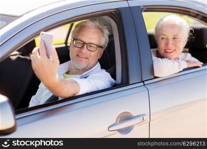 road trip, travel and old people concept - happy senior couple driving in car and taking selfie by smartphone. senior couple in car taking smartphone selfie