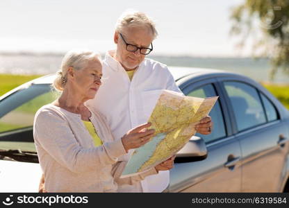 road trip, travel and old people concept - senior couple with car looking for location on map in summer. senior couple with car looking for location on map