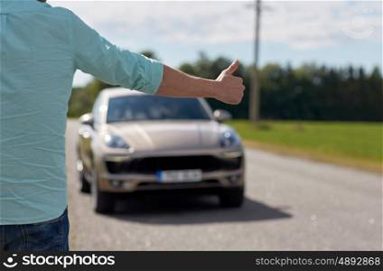 road trip, travel, gesture and people concept - man hitchhiking and stopping car with thumbs up gesture at countryside