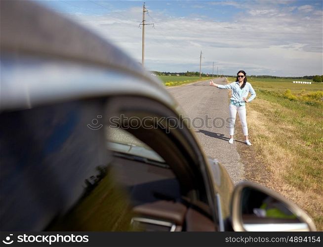 road trip, travel, gesture and people concept - woman hitchhiking and stopping car with thumbs up gesture at countryside