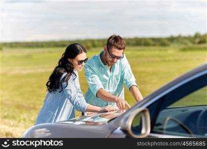 road trip, travel, tourism, family and people concept - happy man and woman searching location on map on car hood outdoors