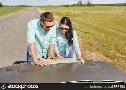 road trip, travel, tourism, family and people concept - happy man and woman searching location on map on car hood outdoors