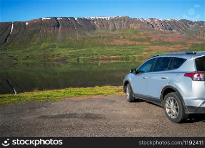 Road trip vacation. SUV car parking on side of lake with mountain background.