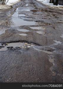 Road with big potholes and muddy puddles, spring time
