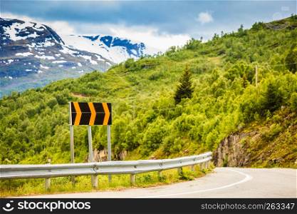 Road with signs running through summer norwegian mountains. Beautiful green natural landscape during sunny weather, forest in background.. Road in Norwegian mountains