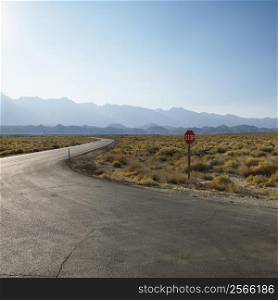 Road with stop sign in barren landscape with mountain in distance.