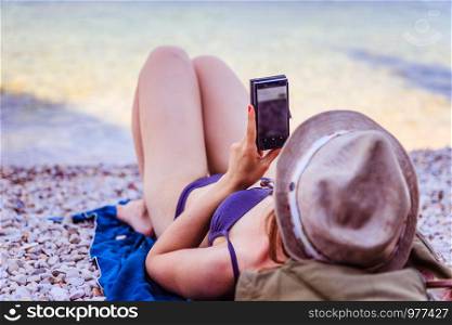 Roaming in the summer holiday: Young girl in bikini is using her smartphone on the beach, Italy