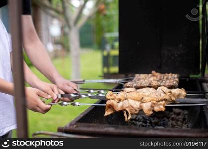 roast meat, food on fire, coals, fire, marinade, nature, fun company, family day, white t-shirt, cooking, cooking, cooking, fatherhood. Hands holding skewers with meat on the magnale