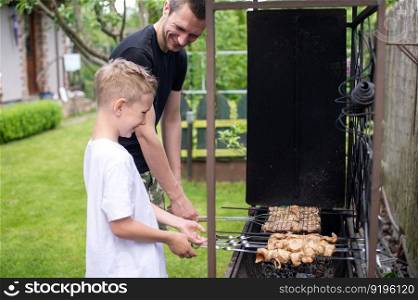 roast meat, food on fire, coals, fire, marinade, nature, fun company, family day, white t-shirt, cooking, cooking, cooking, fatherhood. Cheerful dad and son roast meat on the grill