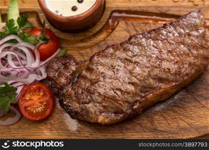 roast meat steak with vegetable garnish and sauce on wooden board