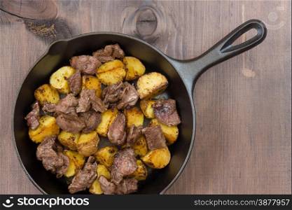 Roast meat with potato in a cast iron skillet on a wooden table