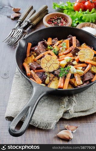 Roast meat with vegetables in a cast iron skillet on a wooden table