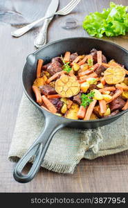 Roast meat with vegetables in a cast iron skillet on a wooden table