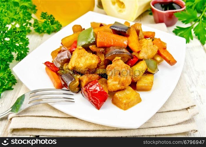 Roast meat, zucchini, eggplant, carrot and sweet pepper with honey, soy sauce and red wine in a plate on a napkin against the background of wooden boards