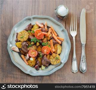 Roast venison with vegetables on a vintage pewter plates and old cutlery on a wooden table