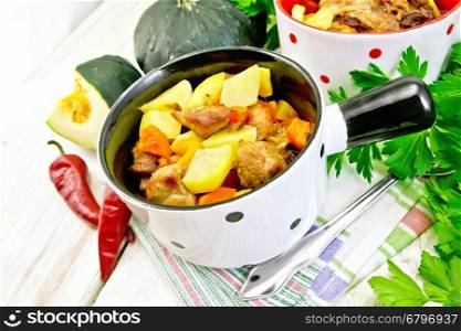 Roast with chicken, potatoes, squash and peppers in two portioned white pot on a towel, spoon, parsley on a wooden boards background