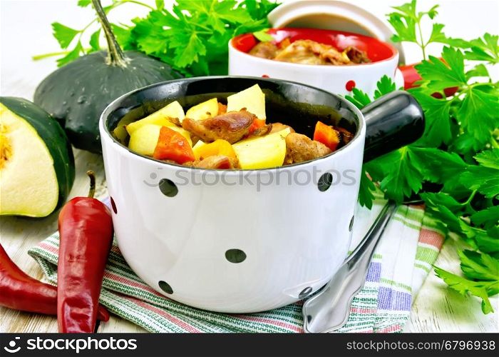 Roast with chicken, potatoes, squash and peppers in two portioned white pot on a towel, spoon, parsley on the background light wooden boards