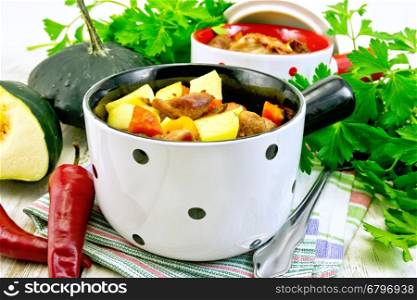 Roast with chicken, potatoes, squash and peppers in two portioned white pot on a towel, spoon, parsley on the background light wooden boards