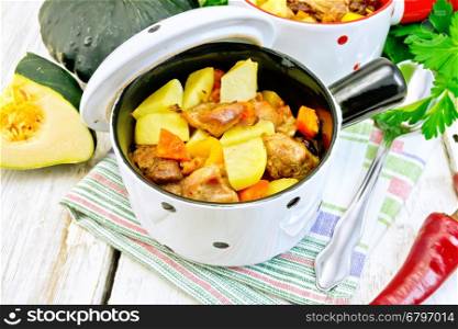 Roast with chicken, potatoes, squash and peppers in two portioned white pot on a napkin, spoon, parsley on the background light wooden boards