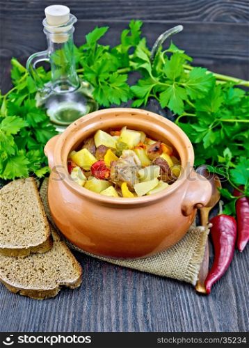 Roast with chicken, potatoes, squash and sweet peppers in a clay pot on a napkin of burlap, bread and parsley on a dark wooden board