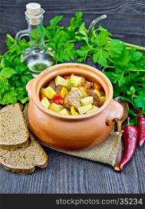 Roast with chicken, potatoes, squash and sweet peppers in a clay pot on a napkin of burlap, bread and parsley on a dark wooden board