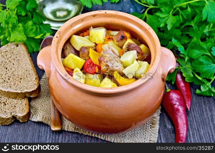 Roast with chicken, potatoes, squash and sweet peppers in a clay pot on a napkin of burlap, bread and parsley on a wooden board background