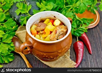 Roast with chicken, potatoes, squash, and sweet peppers in a portion clay pot on a napkin of burlap, spoon, parsley on a wooden boards background