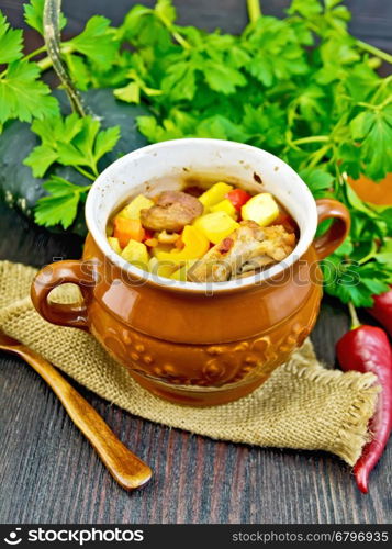 Roast with chicken, potatoes, squash, and sweet peppers in a portion clay pot on a napkin of burlap, spoon, parsley on a dark wooden board