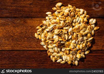 Roasted and salted pumpkin seeds on a wooden board.