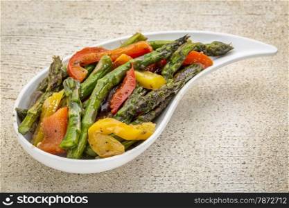 roasted asparagus salad with bell pepper on a teardrop shaped bowl against white painted rustic wood