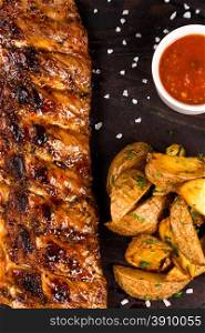 roasted bbq ribs with fry potatoes and souce on dark wooden background