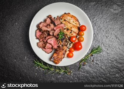 Roasted beef steak fillet and pork chops with herb and spices serve with vegetable on white plate / grilled beef meat slice on black background