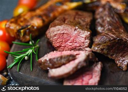 Roasted beef steak fillet with herb and spices served with vegetable on wooden board / grilled beef meat slice on black background
