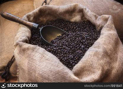 Roasted black coffee beans and an old scoop, in a jute sack. Vintage image of coffee beans in jute packaging. Open jute bag with coffee beans.