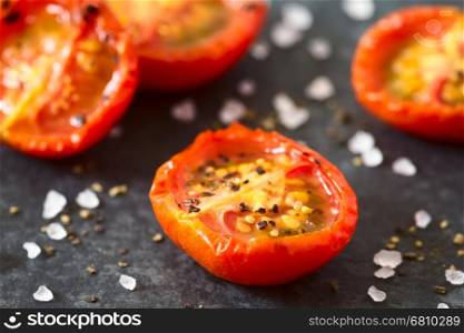 Roasted cherry tomato halves with salt and pepper, photographed closeup on slate with natural light (Very Shallow Depth of Field, Focus one third into the first tomato half)