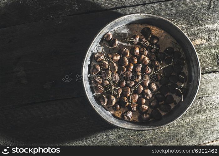 Roasted chestnuts and rosemary. Vintage baking tray. Natural sun rays from window.