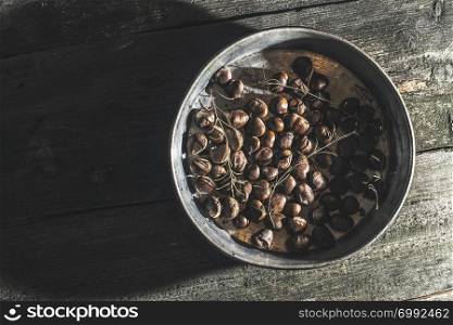 Roasted chestnuts and rosemary. Vintage baking tray. Natural sun rays from window.