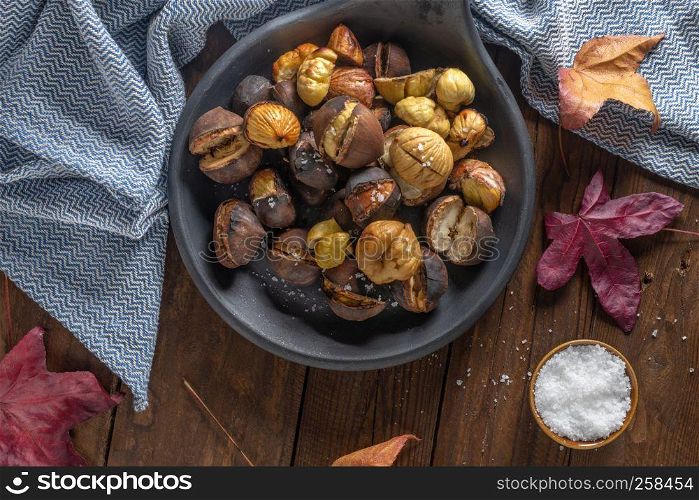 Roasted chestnuts with salt in cast iron grilling pan over rustic wooden board. Top view. Flat lay.