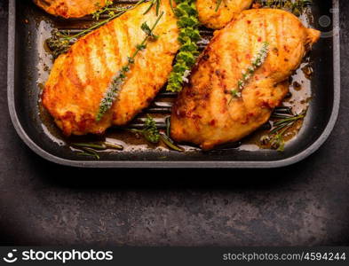 Roasted chicken breast in frying pan with herbs, top view, close up